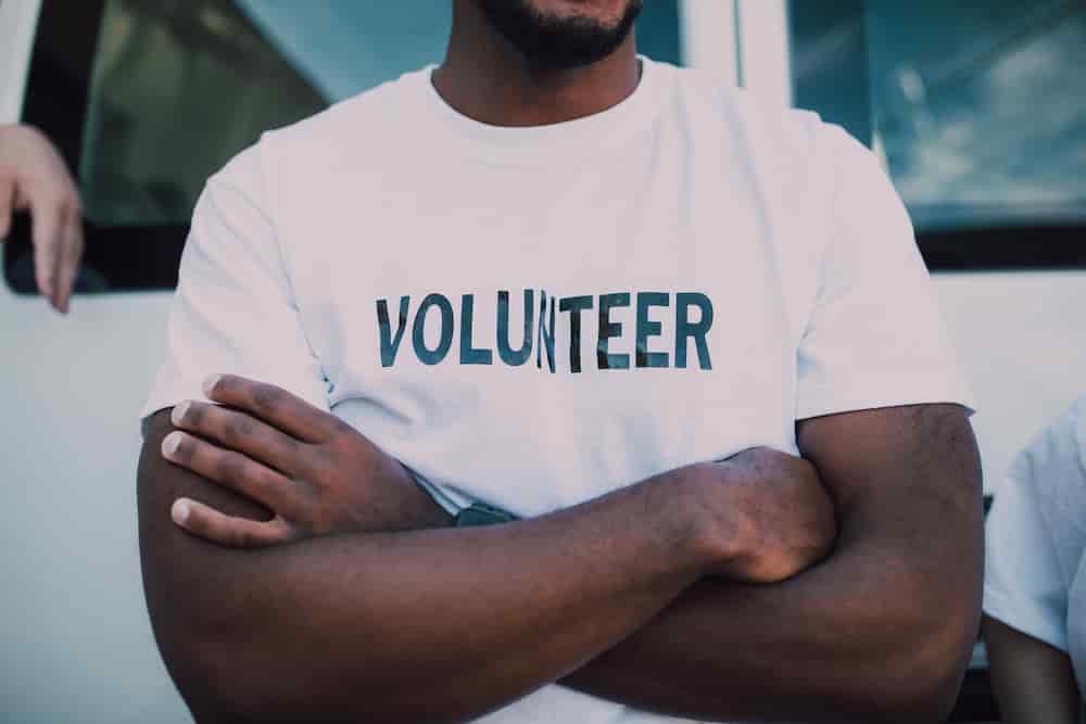 Mann mit verschränkten Armen mit T-Shirt-Beschriftung Volunteer